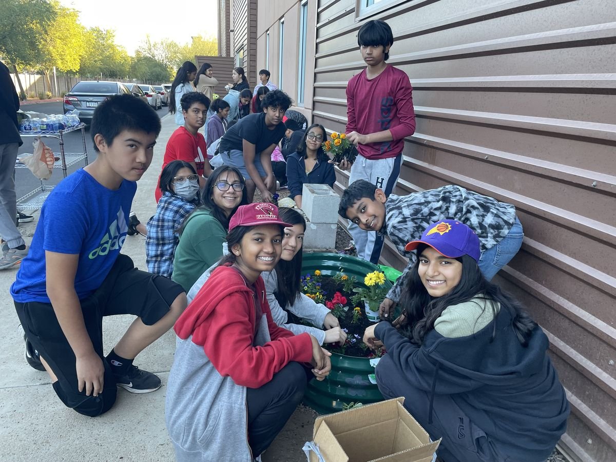 Student volunteers planting flowers in a raised garden bed on the BASIS Chandler campus