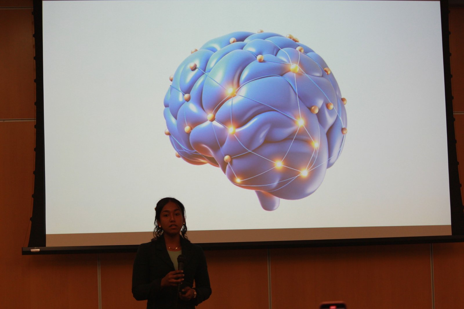 Ariana Rahman speaking in front of a projected brain graphic